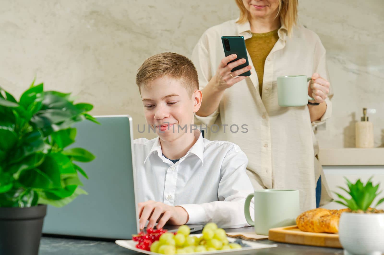 Happy mother and son have healthy breakfast in the kitchen at home. breakfast and digital devices by PhotoTime