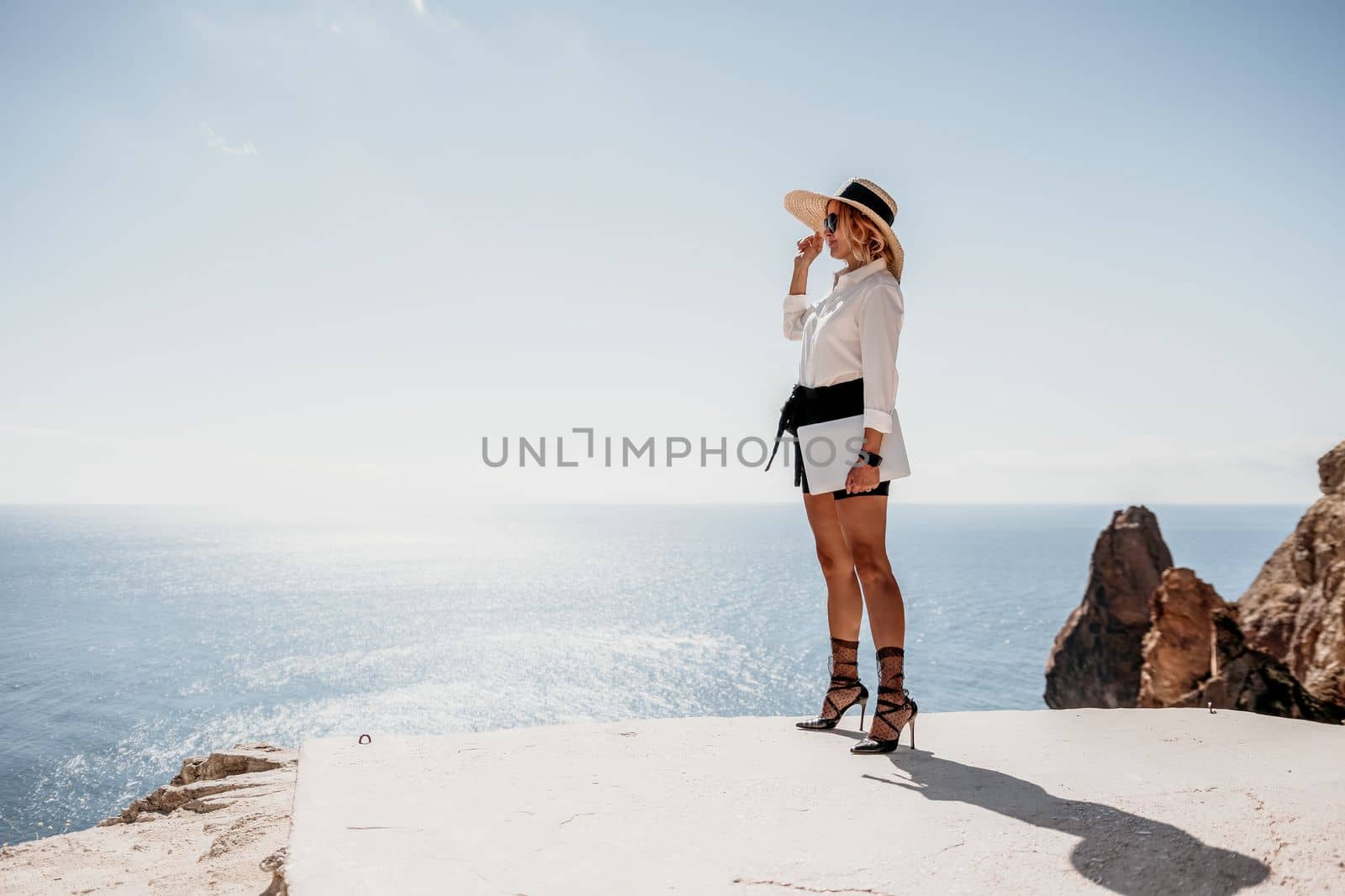 Woman sea laptop. Business woman in yellow hat freelancer with laptop working over blue sea beach. Girl relieves stress from work. Freelance, digital nomad, travel and holidays concept by panophotograph