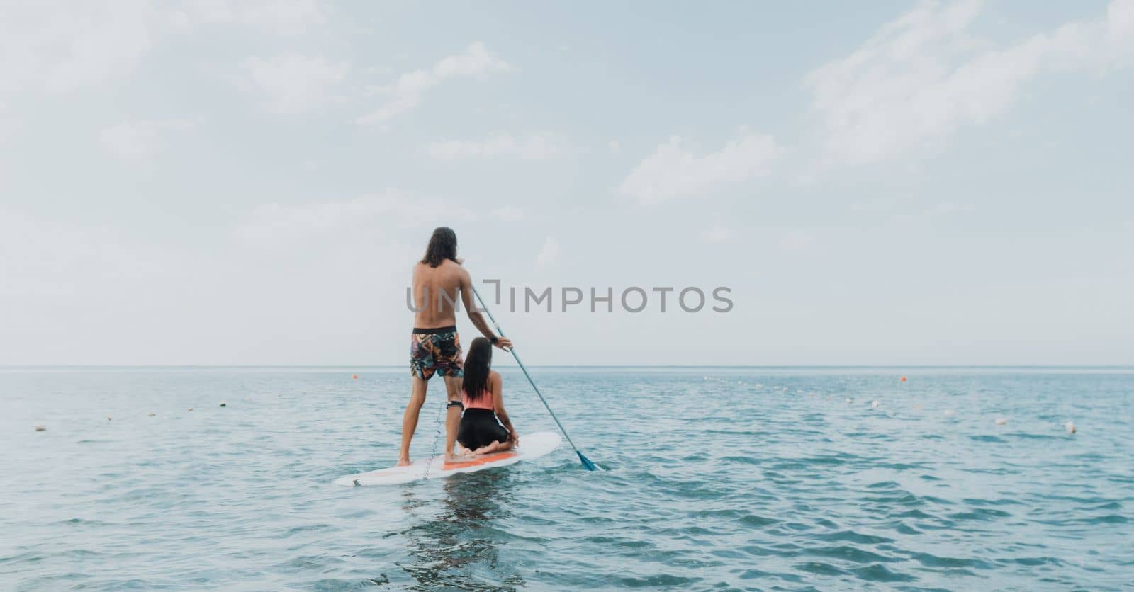 Sea woman and man on sup. Silhouette of happy young woman and man, surfing on SUP board, confident paddling through water surface. Idyllic sunset. Active lifestyle at sea or river