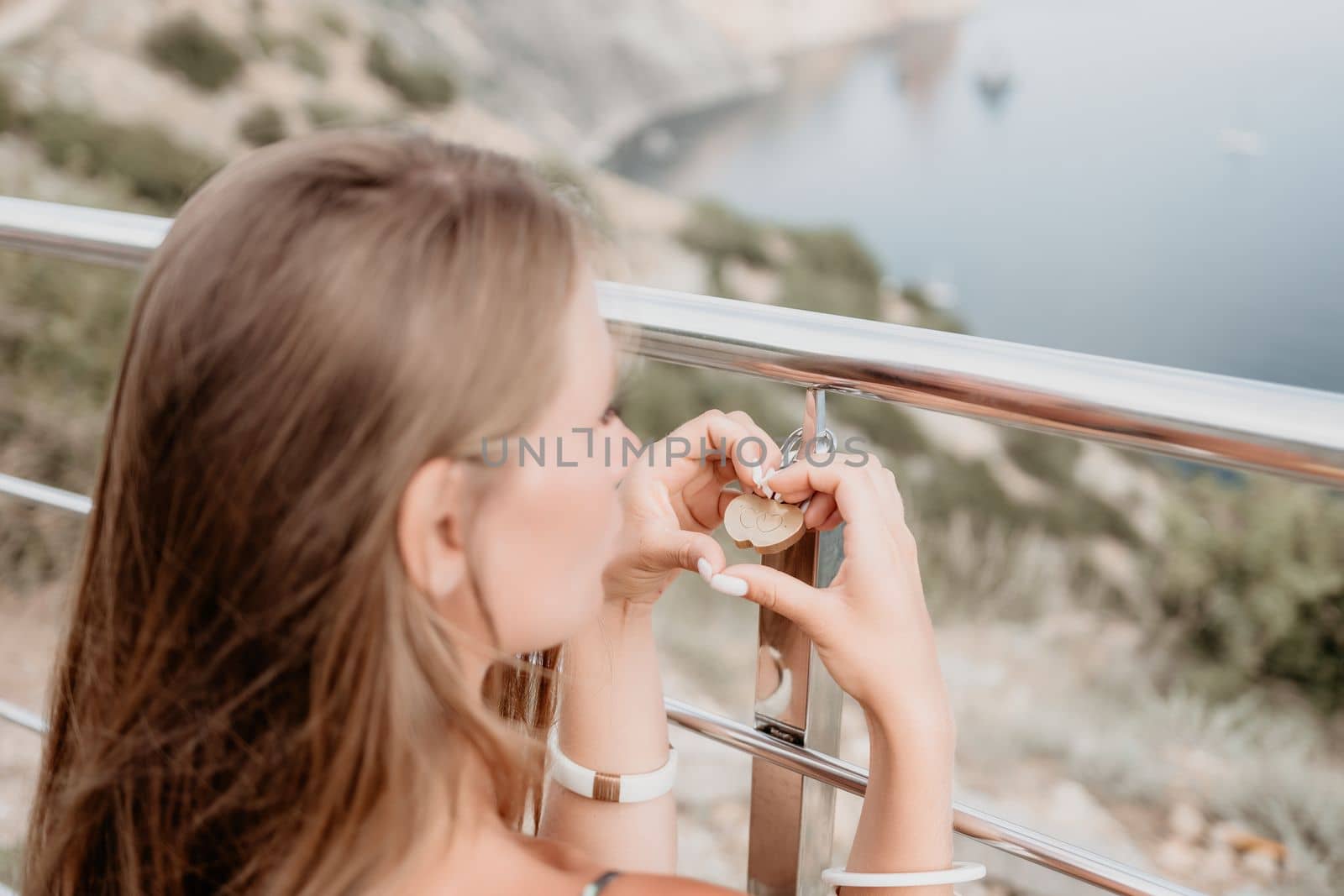 Hand, lock, heart, love, valentines day. Close up view of a woman holding a heart shaped lock that is locked onto a chain link fence.