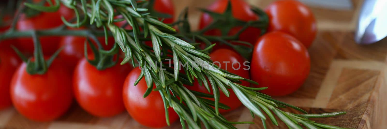 Organic cherry tomatoes with rosemary on wooden board with knife by kuprevich
