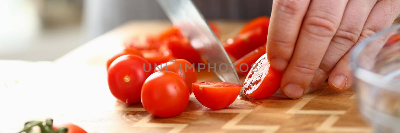 Closeup of man hand cutting tomato on cutting board at home by kuprevich