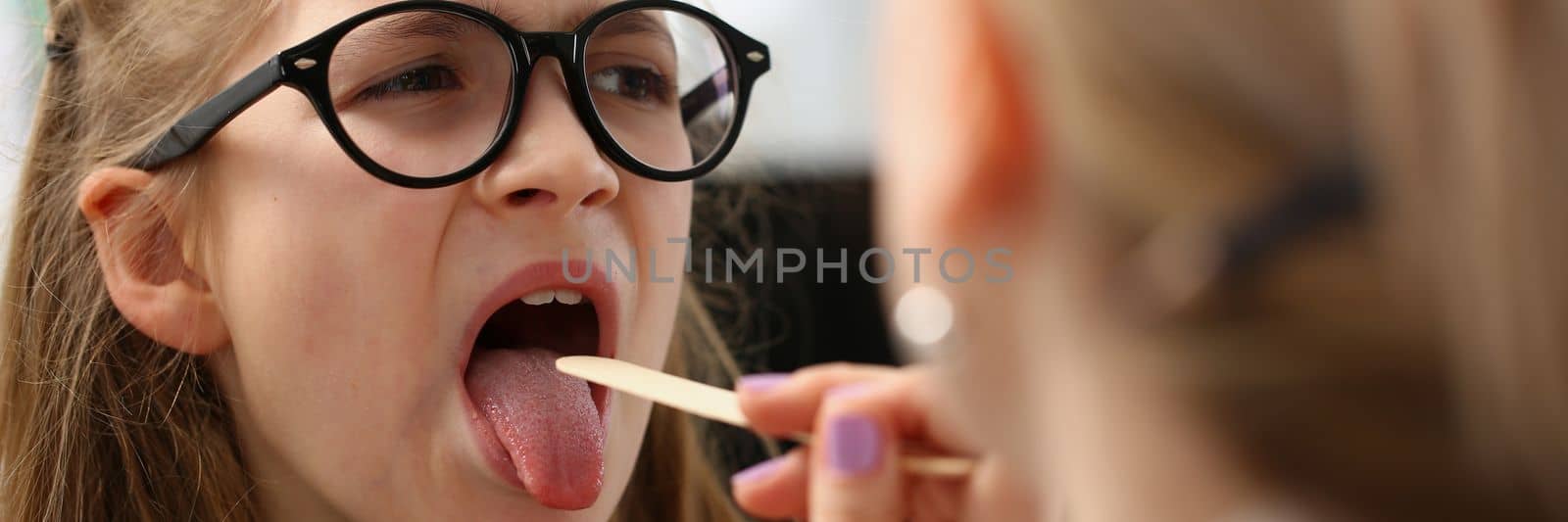 Tonsillitis colds and flu in children with sore throat. Pediatrician woman doctor checks throat of patient girl child visits clinic