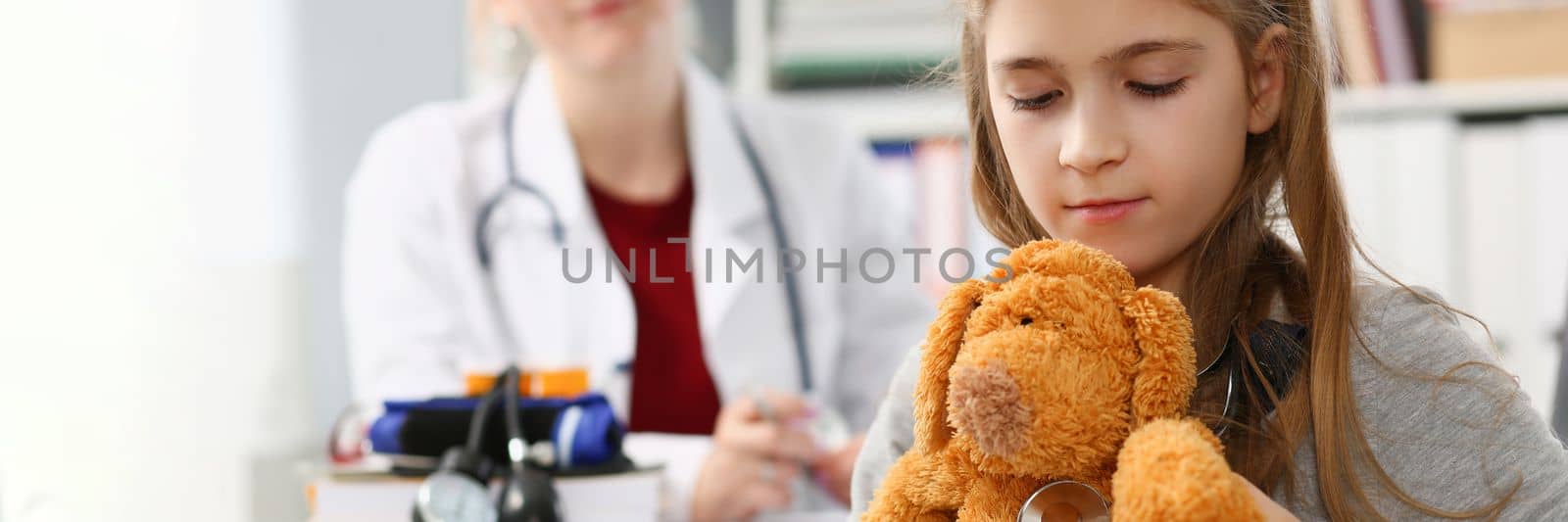 Little girl child holding toy and stethoscope at reception of pediatrician by kuprevich