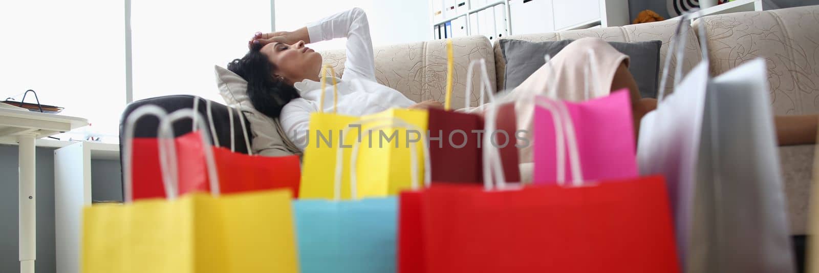 Tired woman sleeping on sofa with bags on floor. Shopping fatigue and stress
