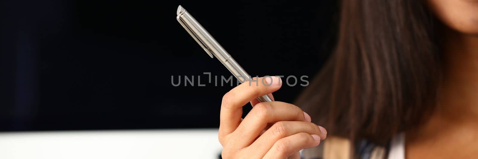 Woman hand holds metal pen on background of workplace. Gesture and sign training and education