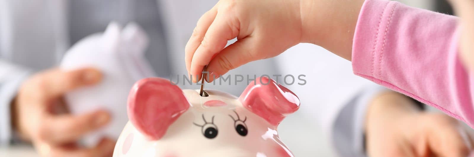 Child hand put a money coin in piggy bank to save money wealth by kuprevich