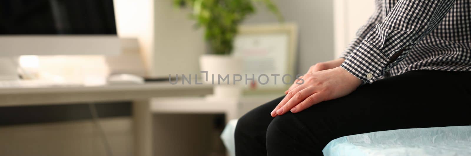 Closeup of young woman sitting on couch with folded hands on knees by kuprevich