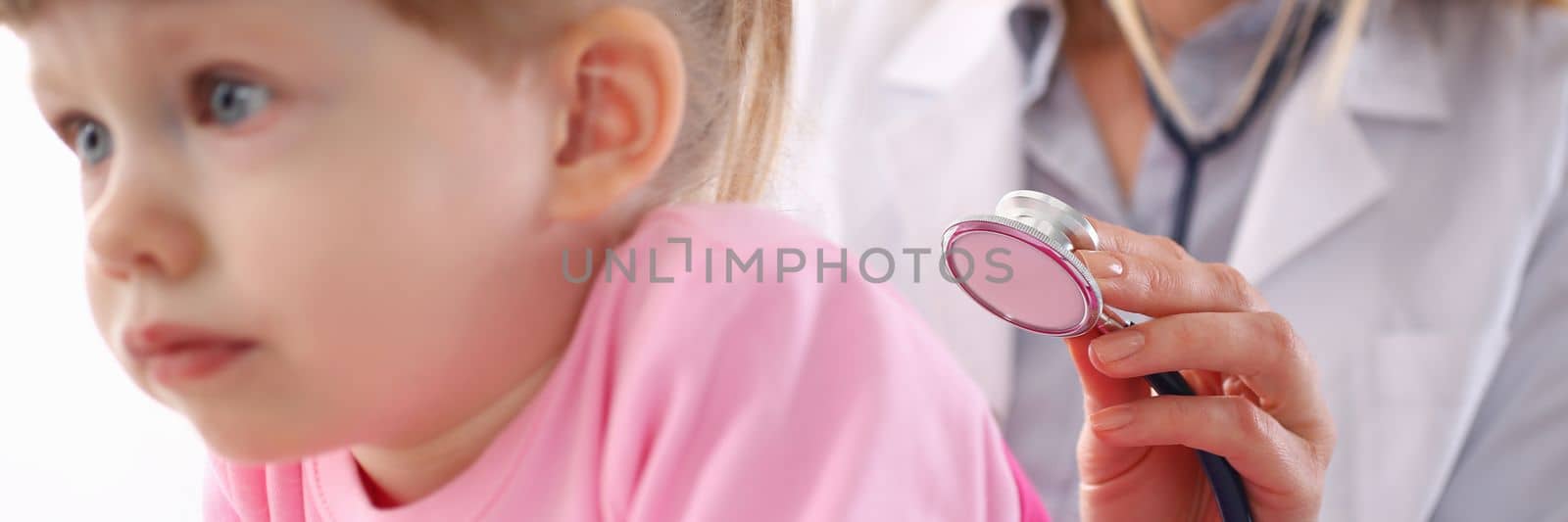 Pediatrician listens to lungs of small child girl with stethoscope by kuprevich