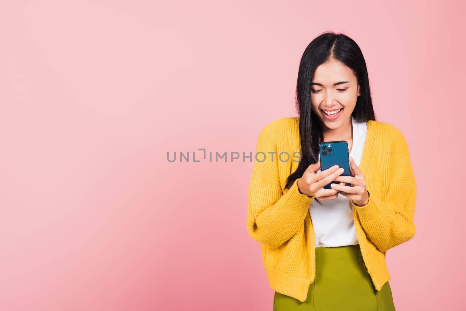 Happy Asian portrait beautiful cute young woman teen smiling excited using smart mobile phone studio shot isolated on pink background, Thai female surprised making winner gesture on smartphone