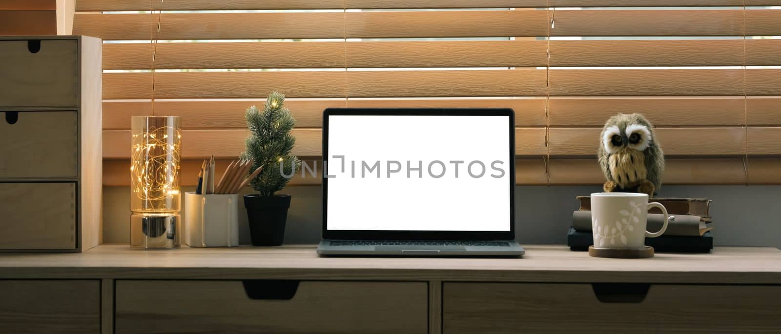Front view laptop computer with white display on wooden counter near blinds window by prathanchorruangsak