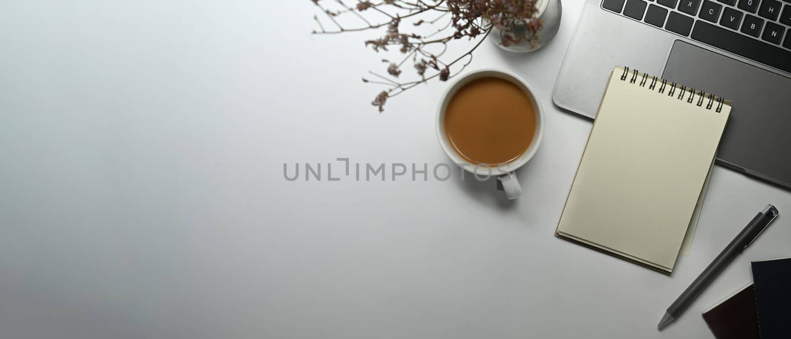 Top view of empty notepad, cup of coffee, laptop and dried flowers on white table. Copy space for your text by prathanchorruangsak