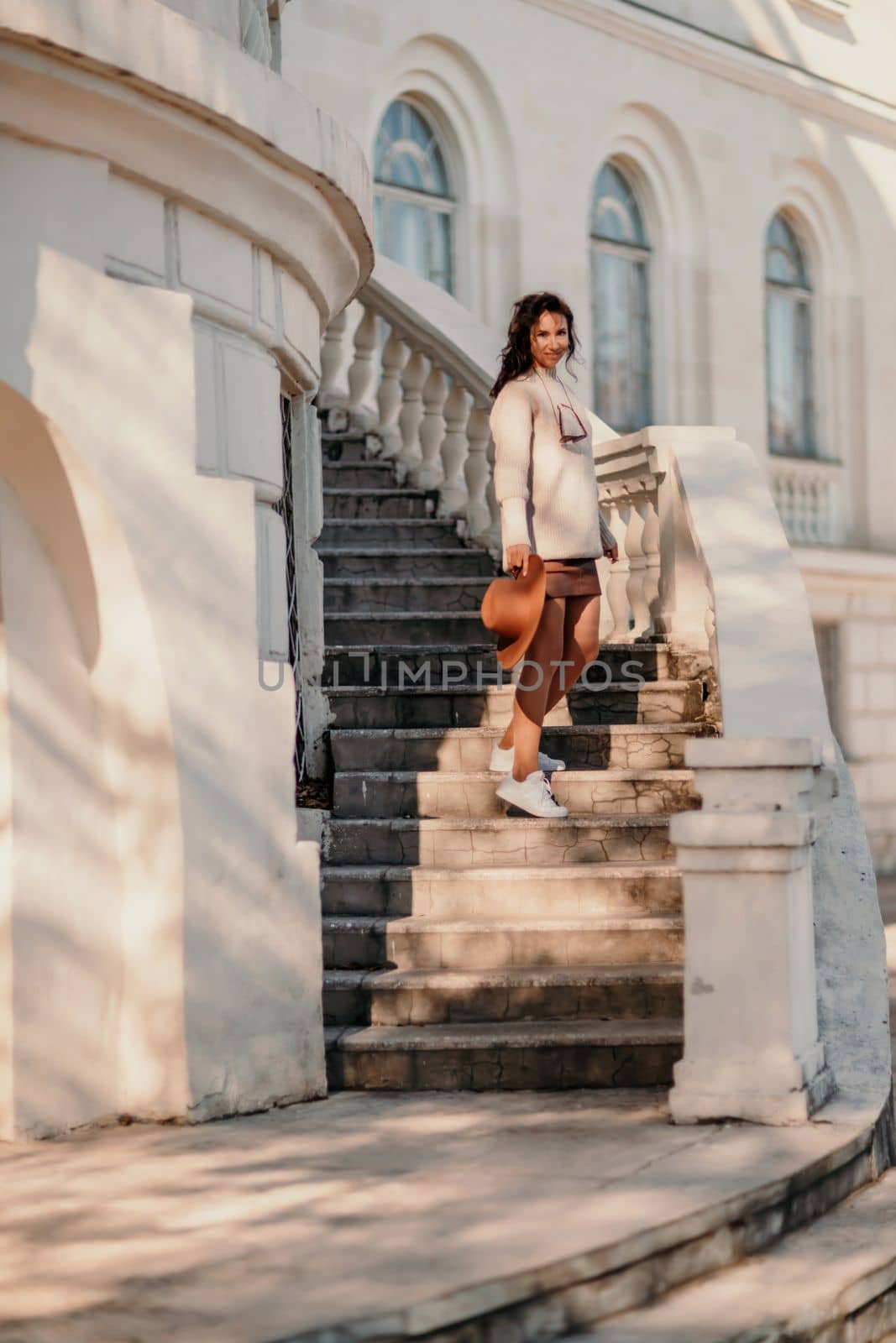 Woman walks in the city, lifestyle. Young beautiful woman in a loose light sweater, brown skirt and sneakers with a hat