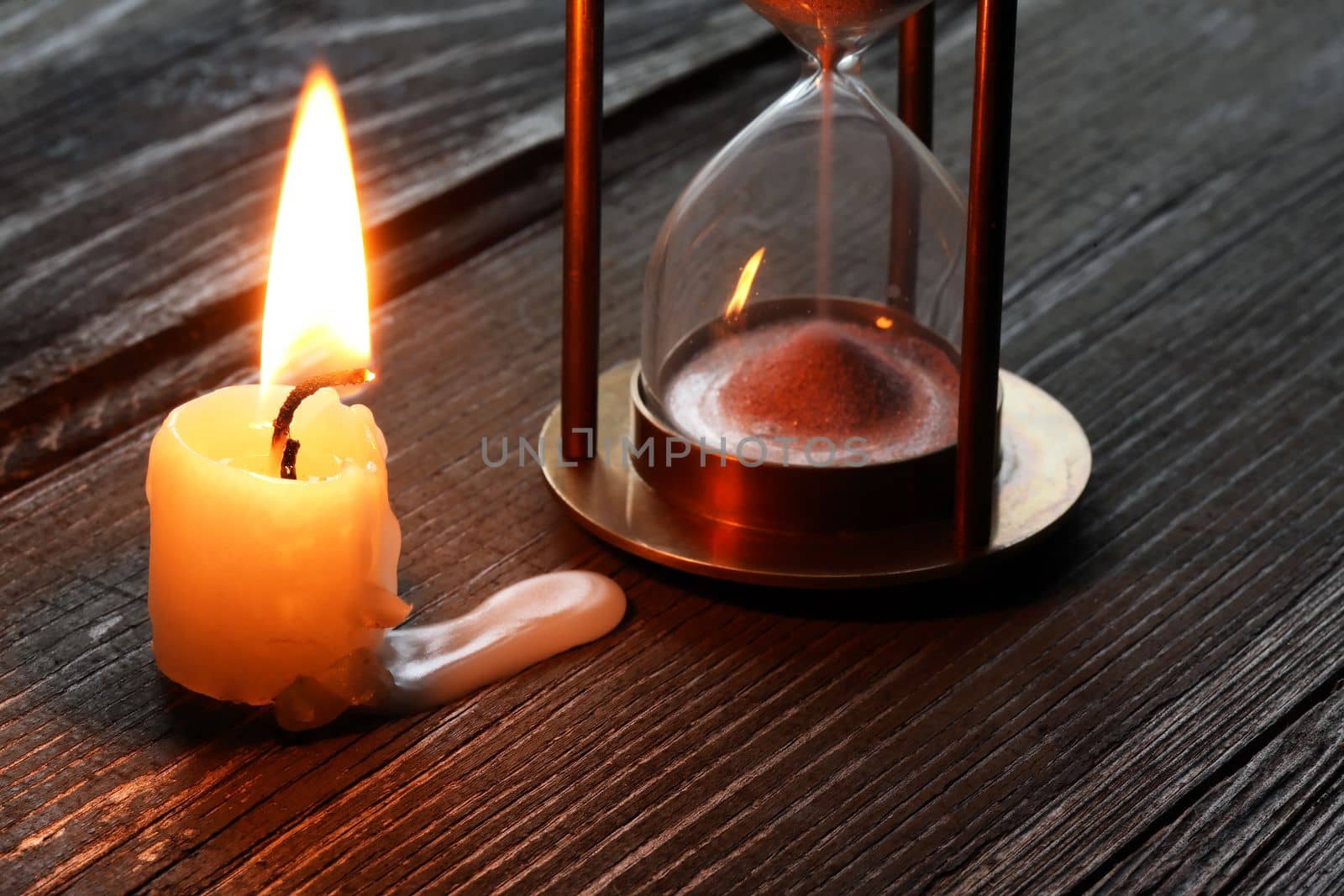 Flighting candle near hourglass on old wooden surface