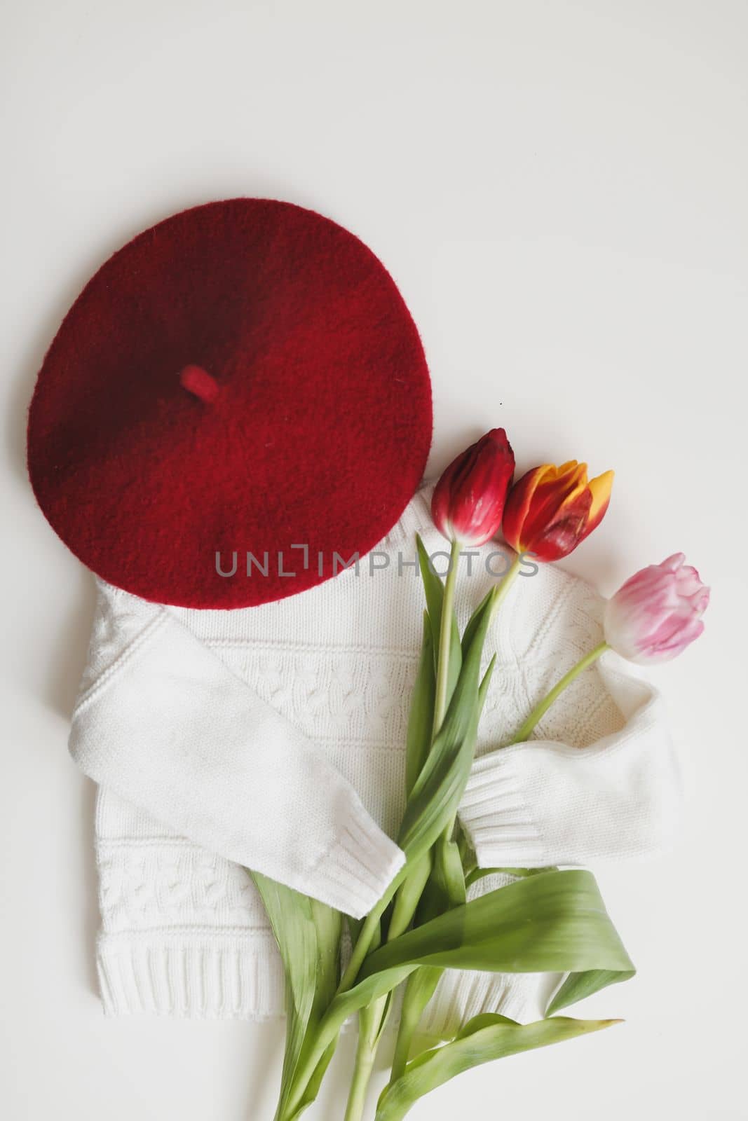 Flat lay white knitted sweater, red hat and bouquet of fresh tulips. Sunday relaxing, vintage mood and lifestyle concept. Cozy spring composition by paralisart