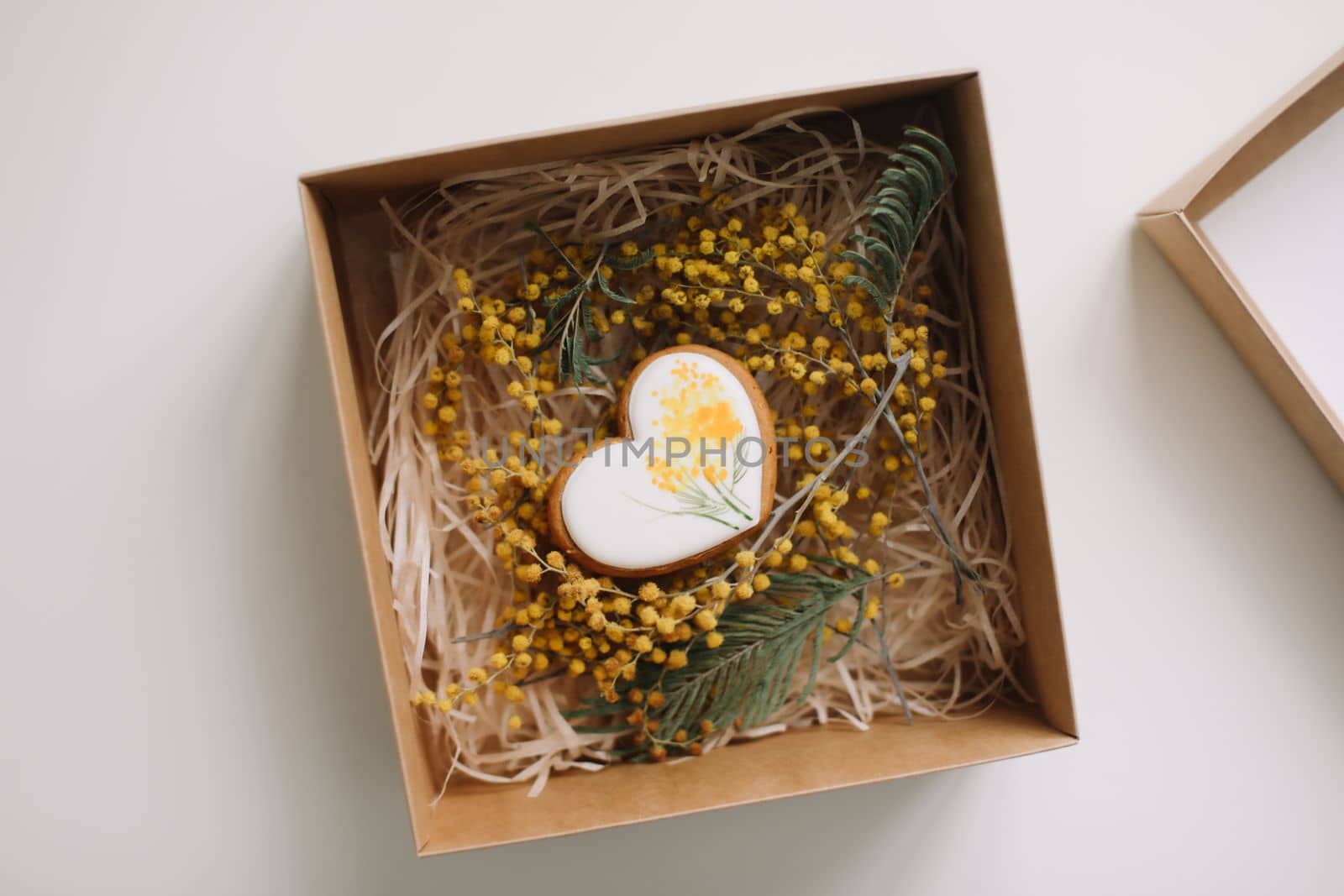 Easter gingerbread cookie in shape of a heart in a gift box with colorful yellow mimosa flowers. Eastet, Spring, April card or banner. Top view.