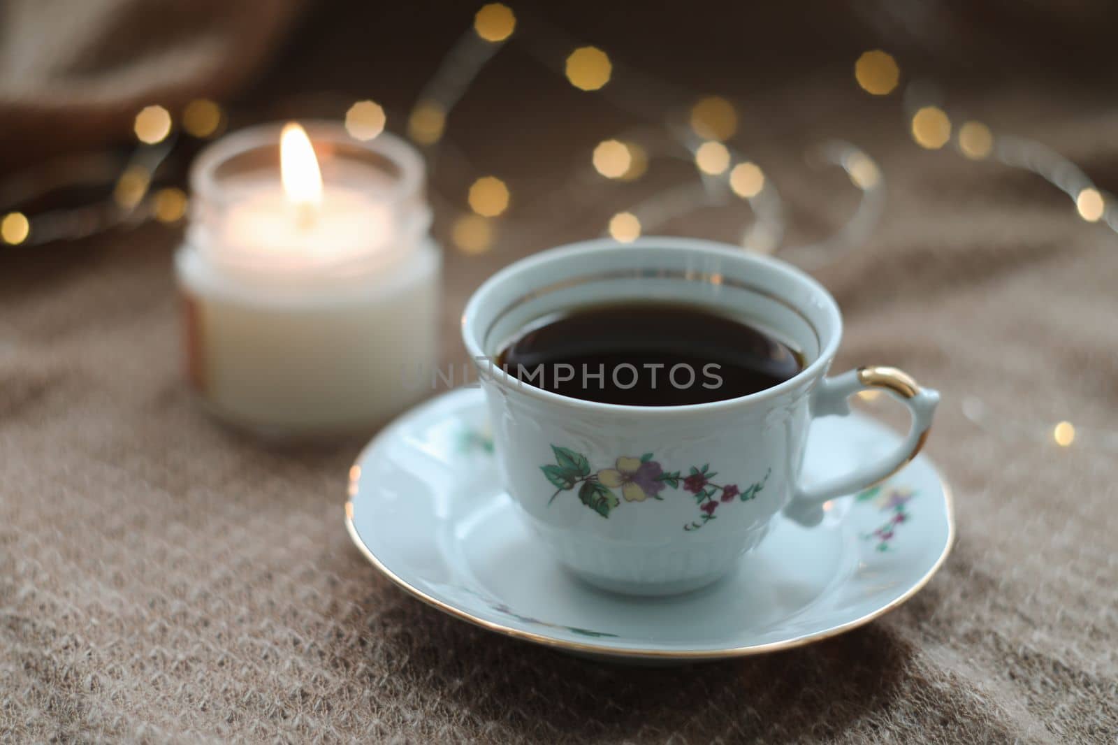 Details of still life in home interior of living room. Sweater, cup of tea, cotton, cozy, candle. Mug, candles and a garland bokeh on a dark cozy background. Decoration, vintage with glow bokeh