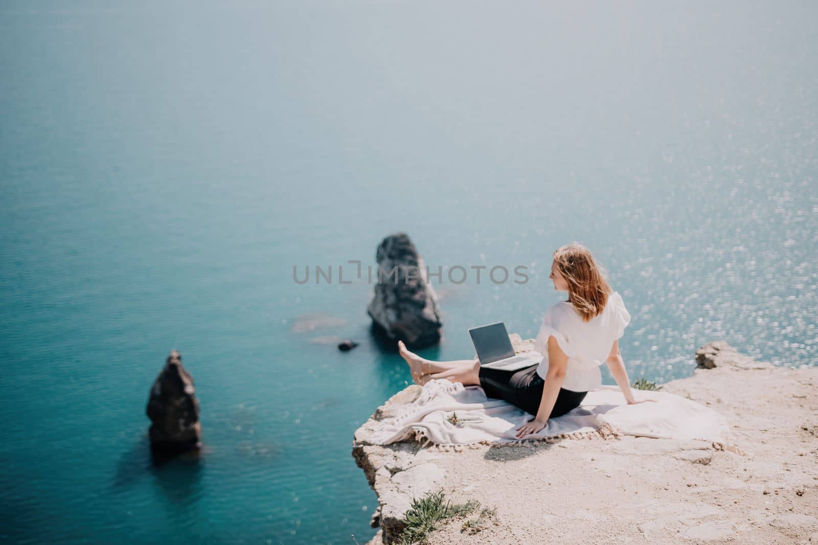 Woman sea laptop. Successful business woman working on laptop by the sea. Pretty lady typing on computer at summer day outdoors. Freelance, digital nomad, travel and holidays concept. by panophotograph
