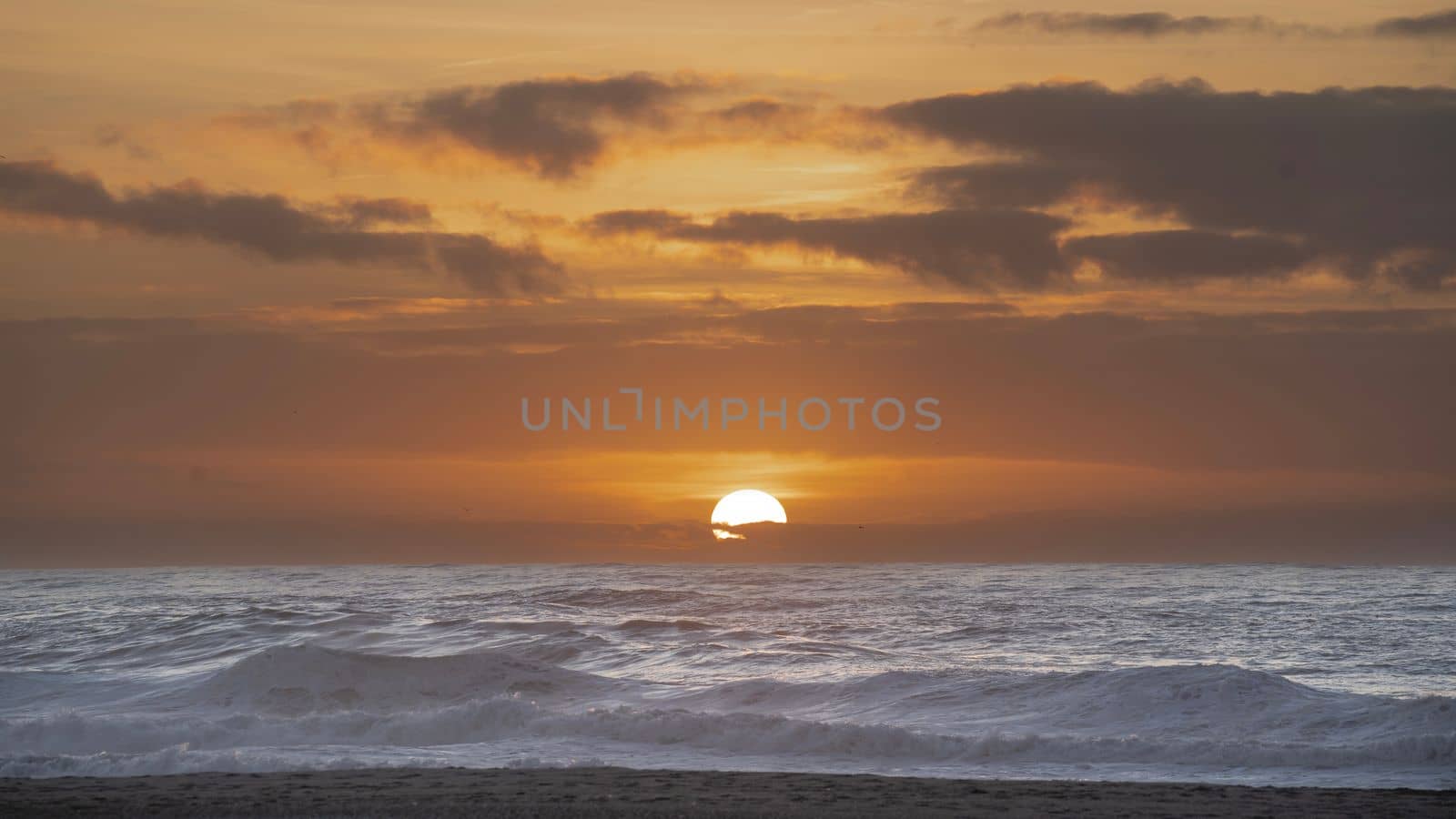 Farewell to the Day with sun hiding in the horizon behind sea water in Portugal beach near porto.