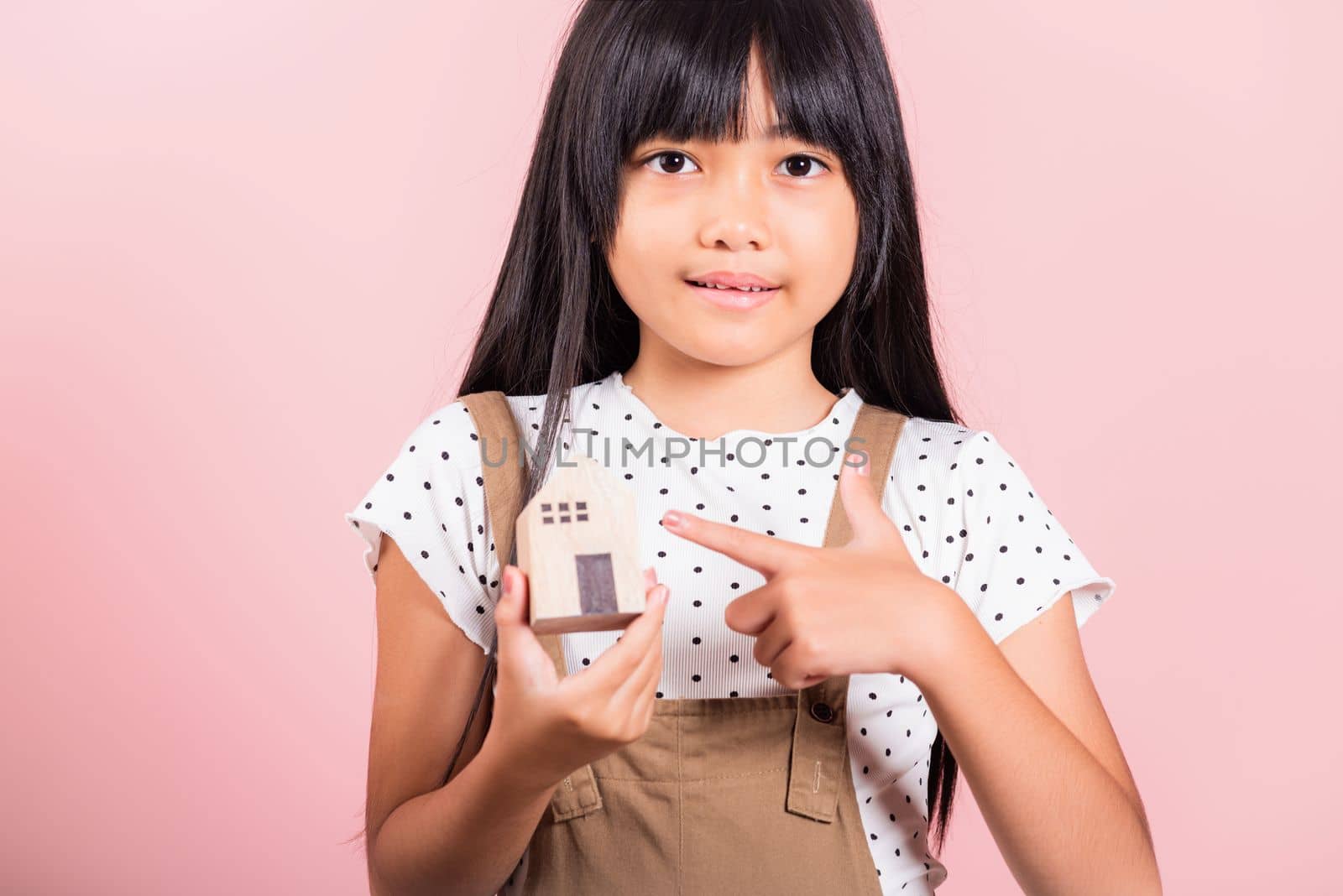 Asian little kid 10 years old hold wood house model on hands at studio shot isolated on pink background, Happy child girl with home model