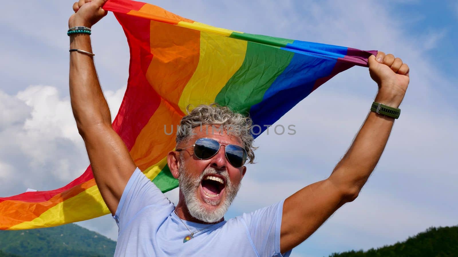 Gay gray-haired holds LGBT flag against a sky by OksanaFedorchuk