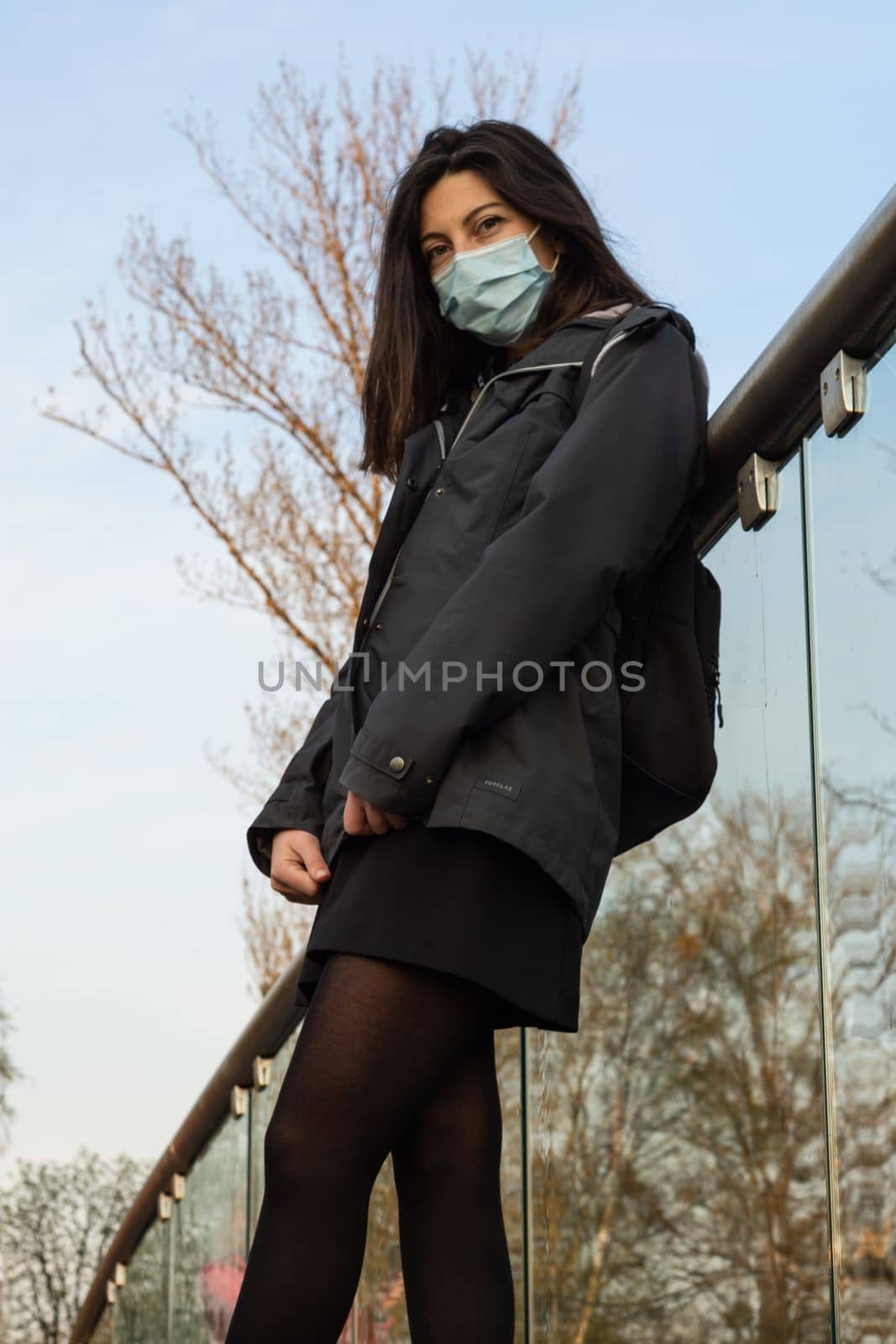 Portrait of happy young woman wearing protective face medical mask standing in park at sunset during spring. High quality photo