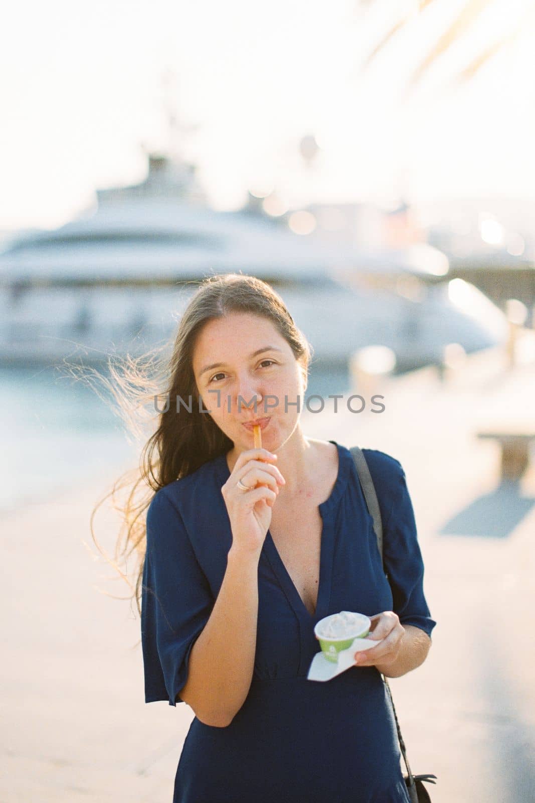 Young woman eating ice cream with a spoon from a cup on the pier. High quality photo
