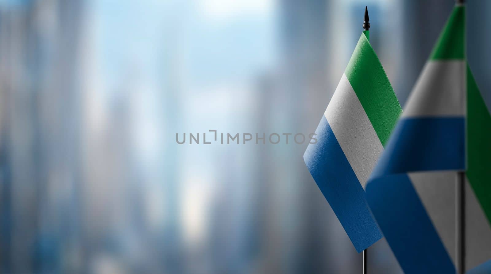 Small flags of the Sierra Leone on an abstract blurry background.