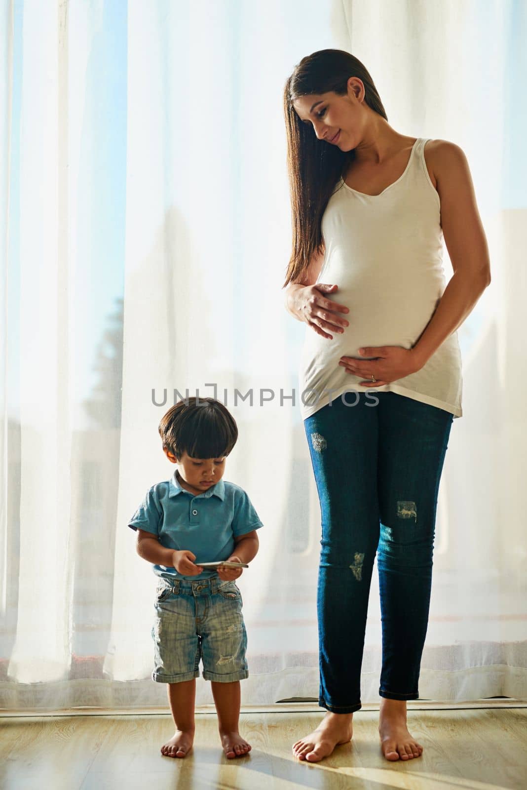 Wireless technology makes a great babysitter. a pregnant woman looking at her little boy while he plays with a smartphone