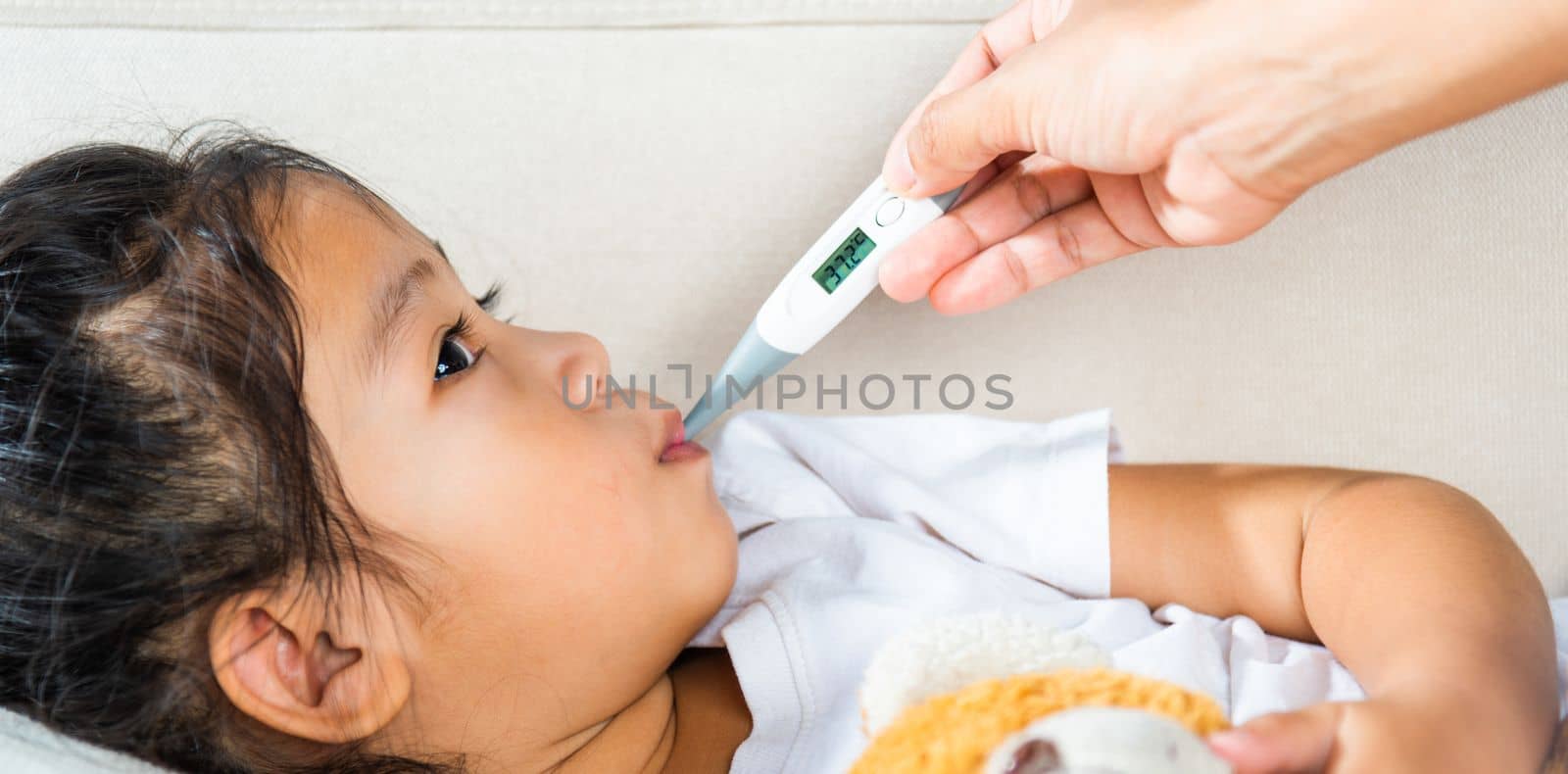 Sick kid. Mother parent checking temperature of her sick daughter with digital thermometer in mouth, child laying in bed taking measuring her temperature for fever and illness, healthcare