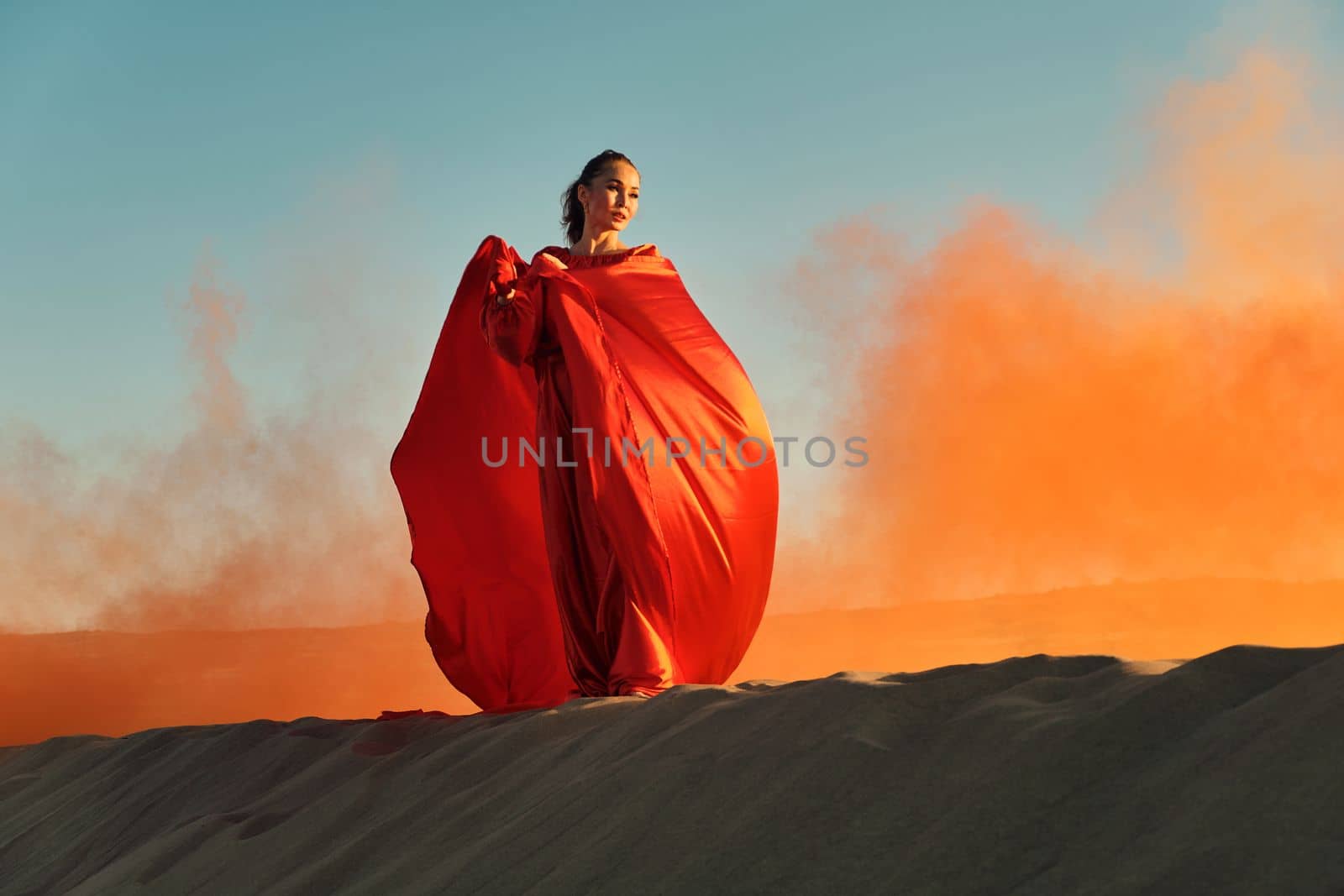 Woman in red dress dancing in the desert at blue sky