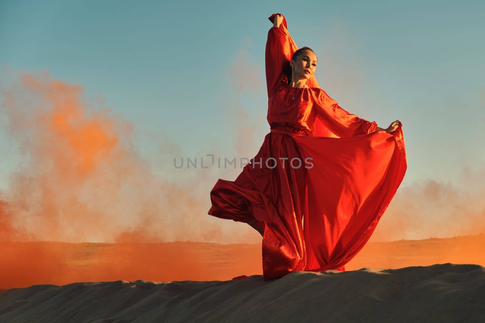 Woman in red dress dancing in the desert at blue sky