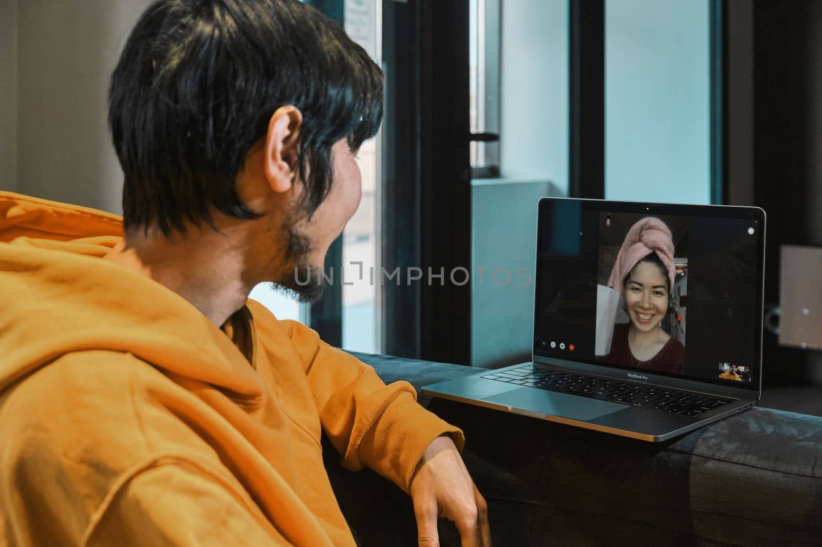 An Asian guy sits in a small office and communicates via video link through a laptop with his girlfriend. The concept of online communication, quarantine, distance.