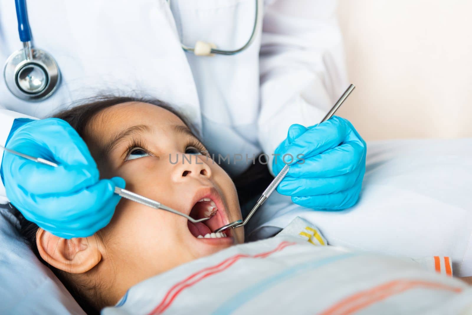 Doctor examines oral cavity of little child uses mouth mirror to checking teeth cavity by Sorapop