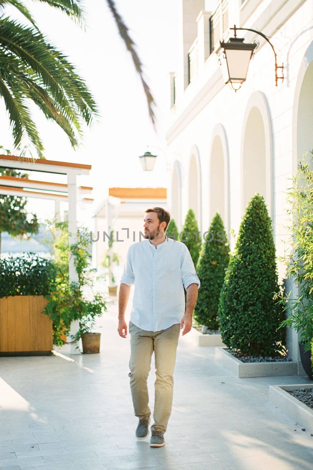 Young man walks down the street past a building with arches and tubed trees. High quality photo