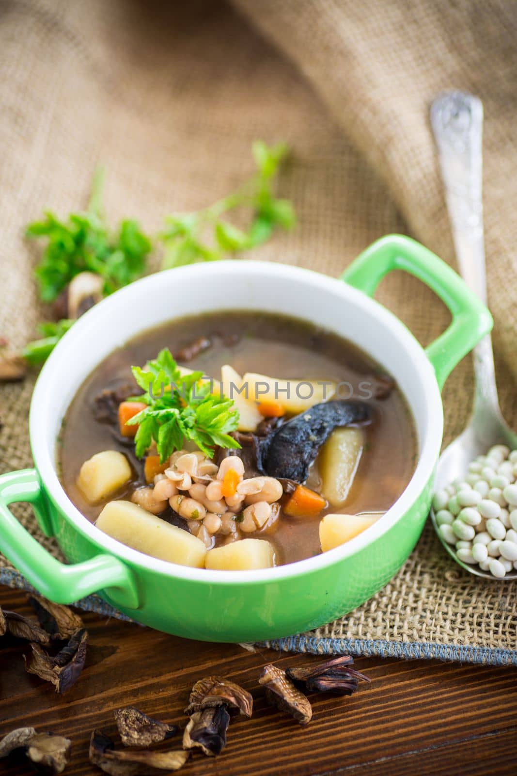 mushroom hot soup with beans in a bowl, on a rustic burlap tablecloth.