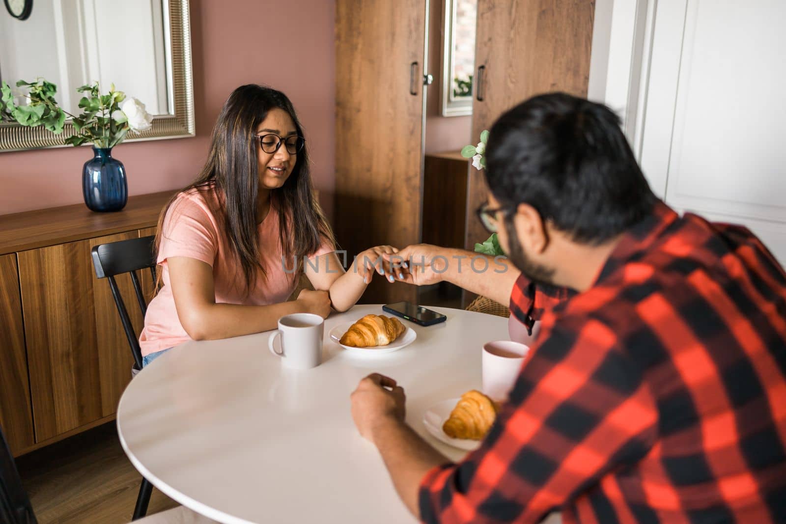 Young diverse loving couple eating croissant and talks together at home in breakfast time. Communication and relationship