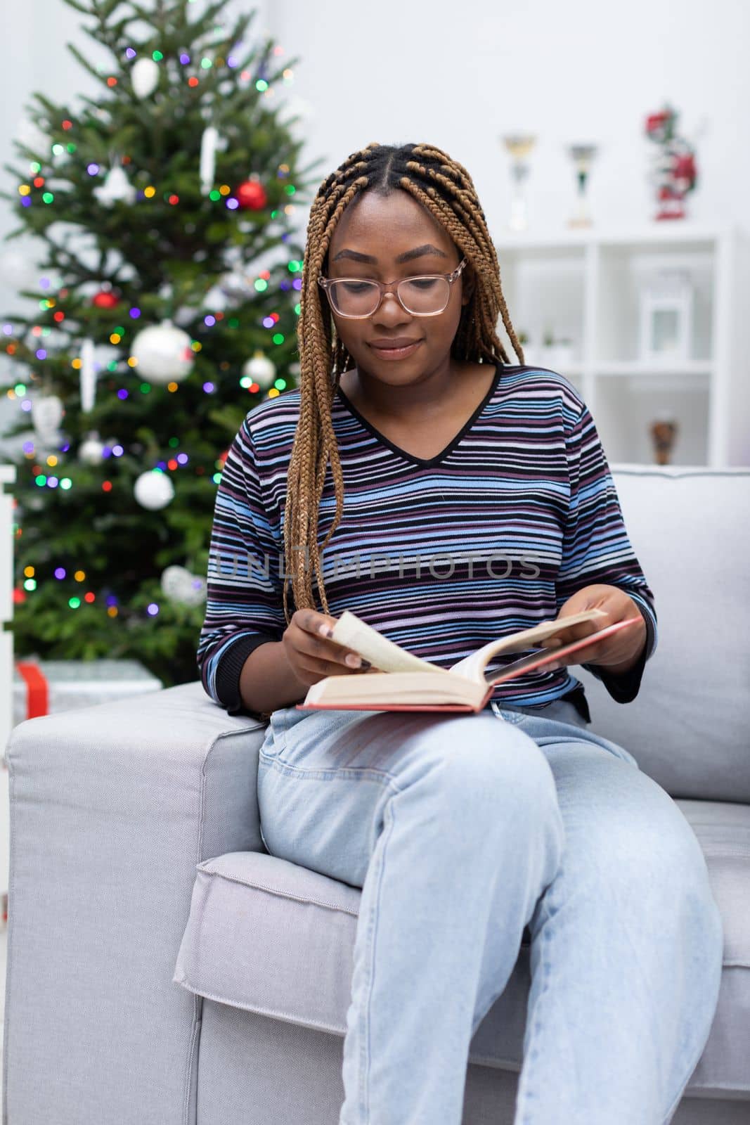 Before Christmas Eve, a dark-skinned girl reads stories in a book in her free time. Christmas decoration of the living room.