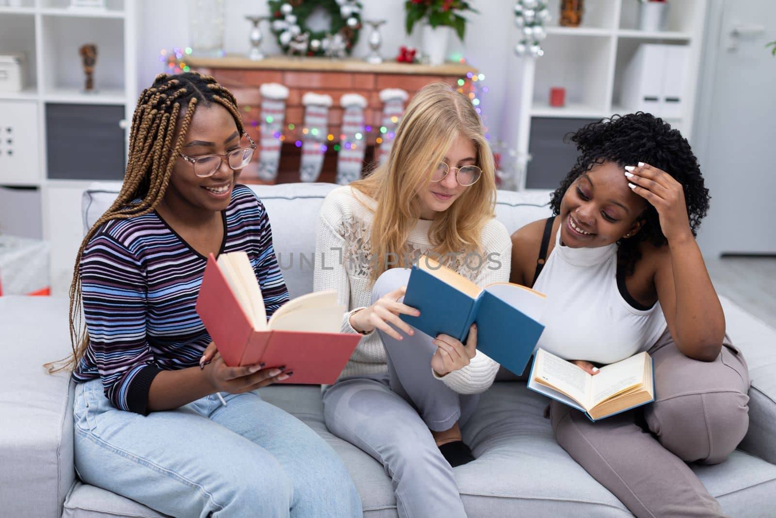 Girls read funny passages in the book and show them to each other. Christmas decoration. Smiling faces of female students.