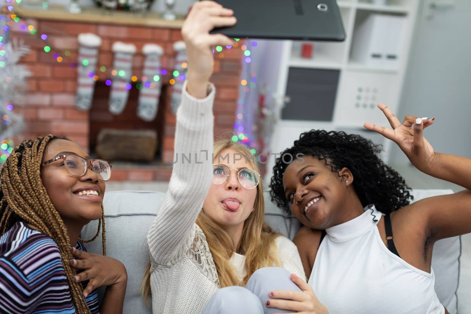 Friends take a selfie together by the decorated fireplace for Christmas. Friends from Africa and Europe.