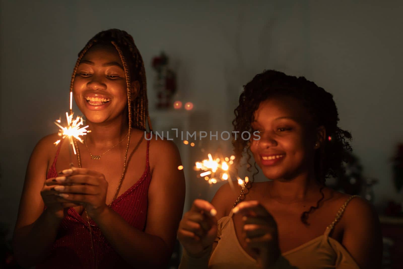 While celebrating the new year, two dark-skinned girls hold burning cold fires.