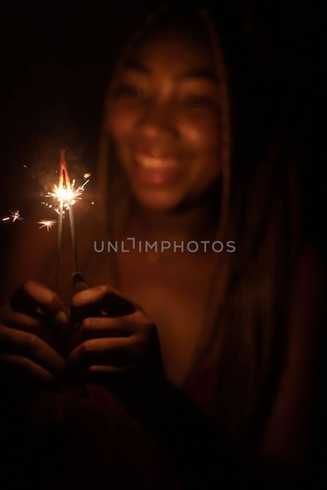 A girl with African beauty during the night of New Year's Eve lit cold fires and holds them in her hand. A happy and smiling student.