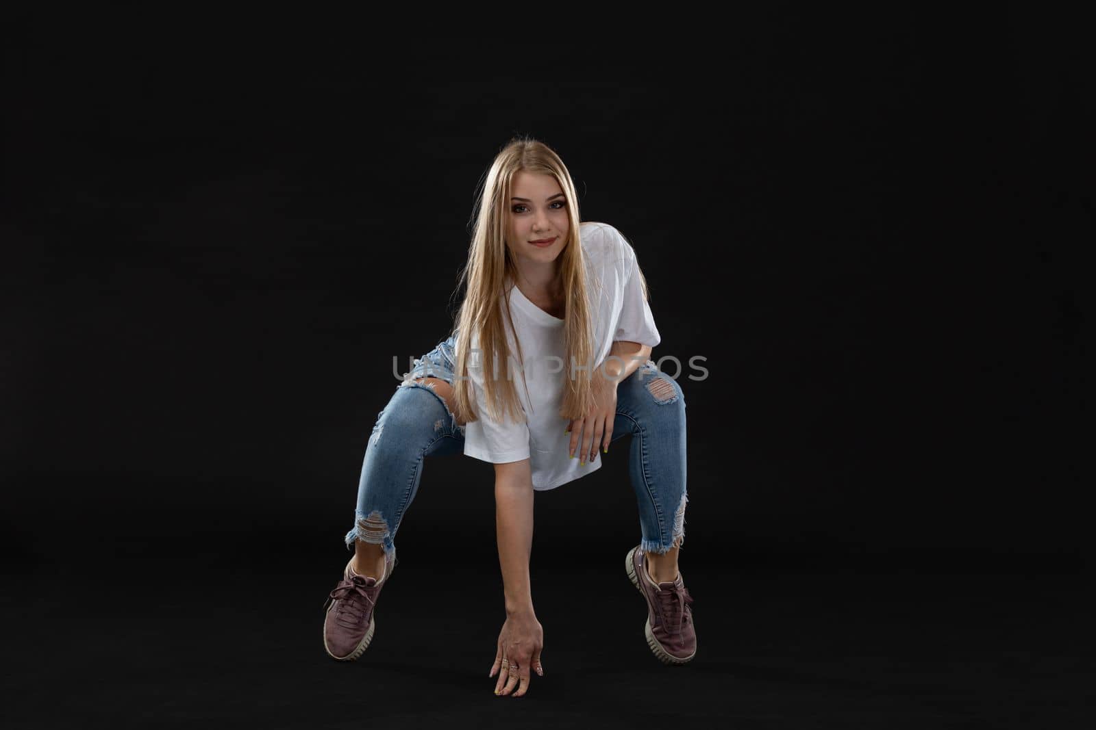 Dance figure. Teenage girl squatting facing the camera propped up on one arm. A young professional dancer.