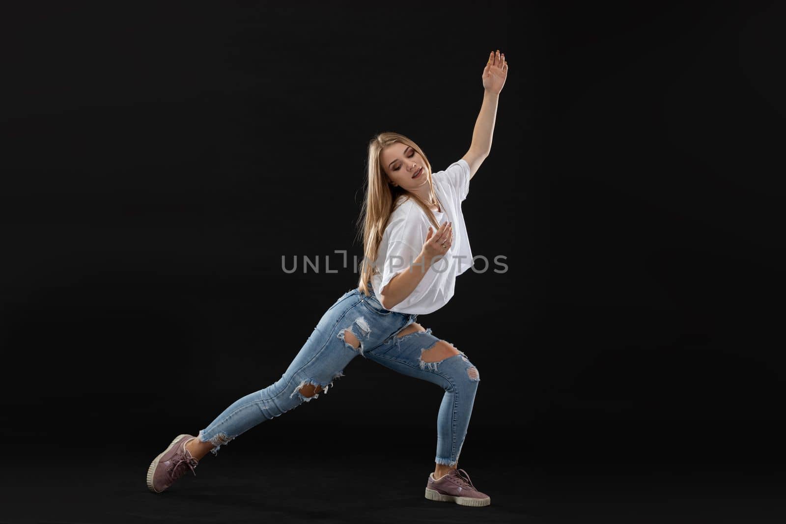 Dance pose. A teenage dancer stands wide apart and places her hands delicately. She looks down. A young professional dancer.