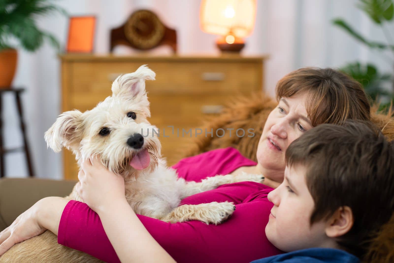 The shaggy dog is held in her arms by her mother and her son cuddles up to her and looks at the beloved pet .