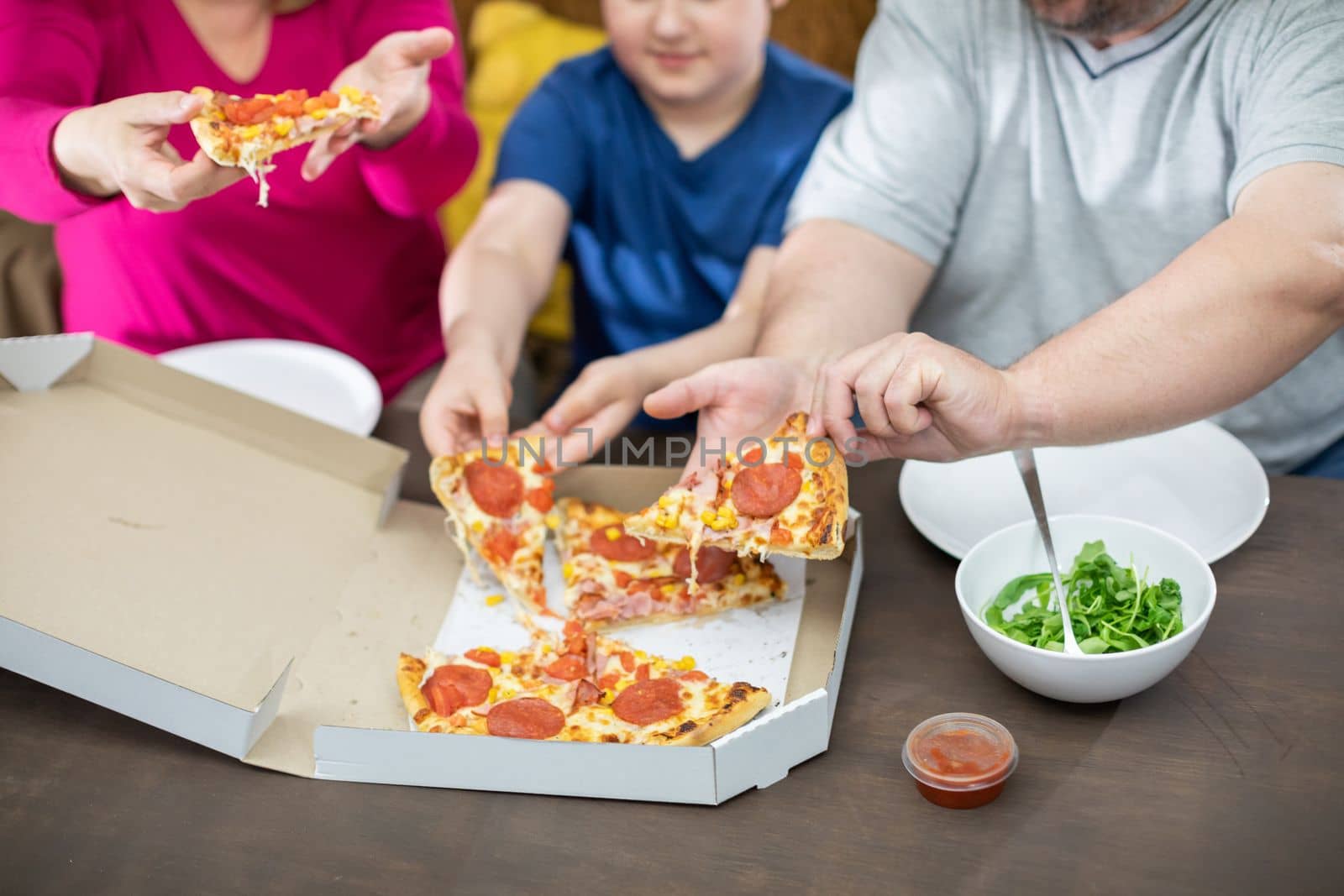 Mother, Father and son treat themselves to hot and fragrant slices of pizza from a box.