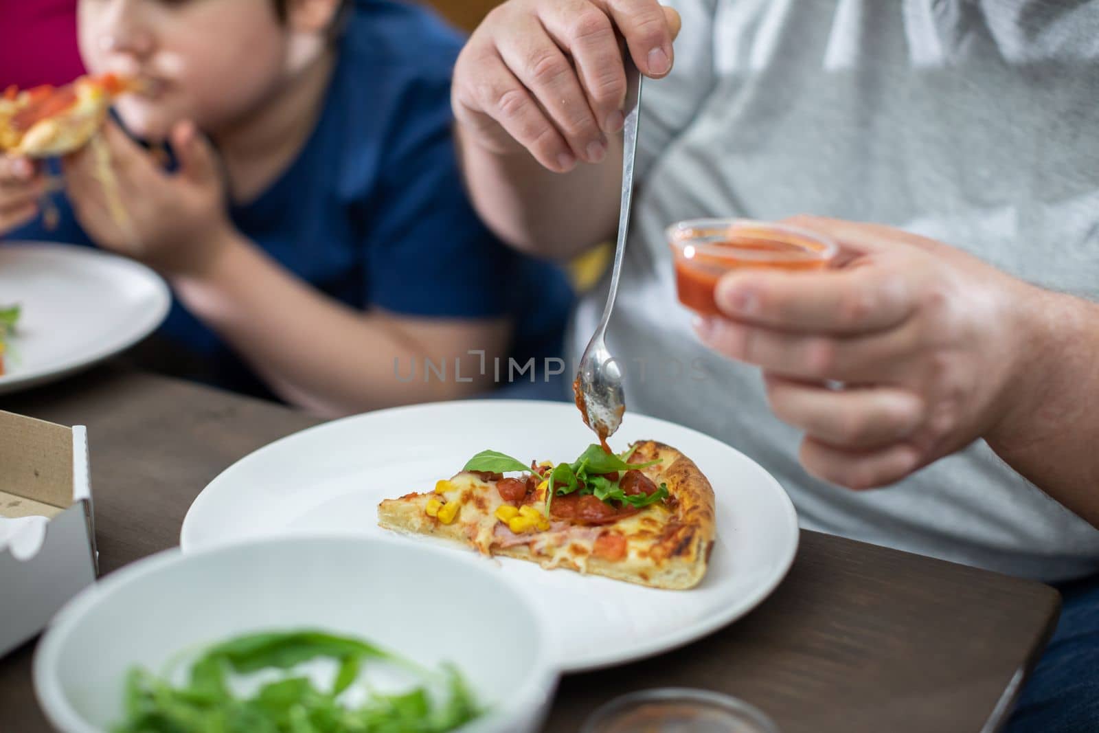 The wife stands and watches as the husband puts tomato sauce on a piece of delicious pizza.