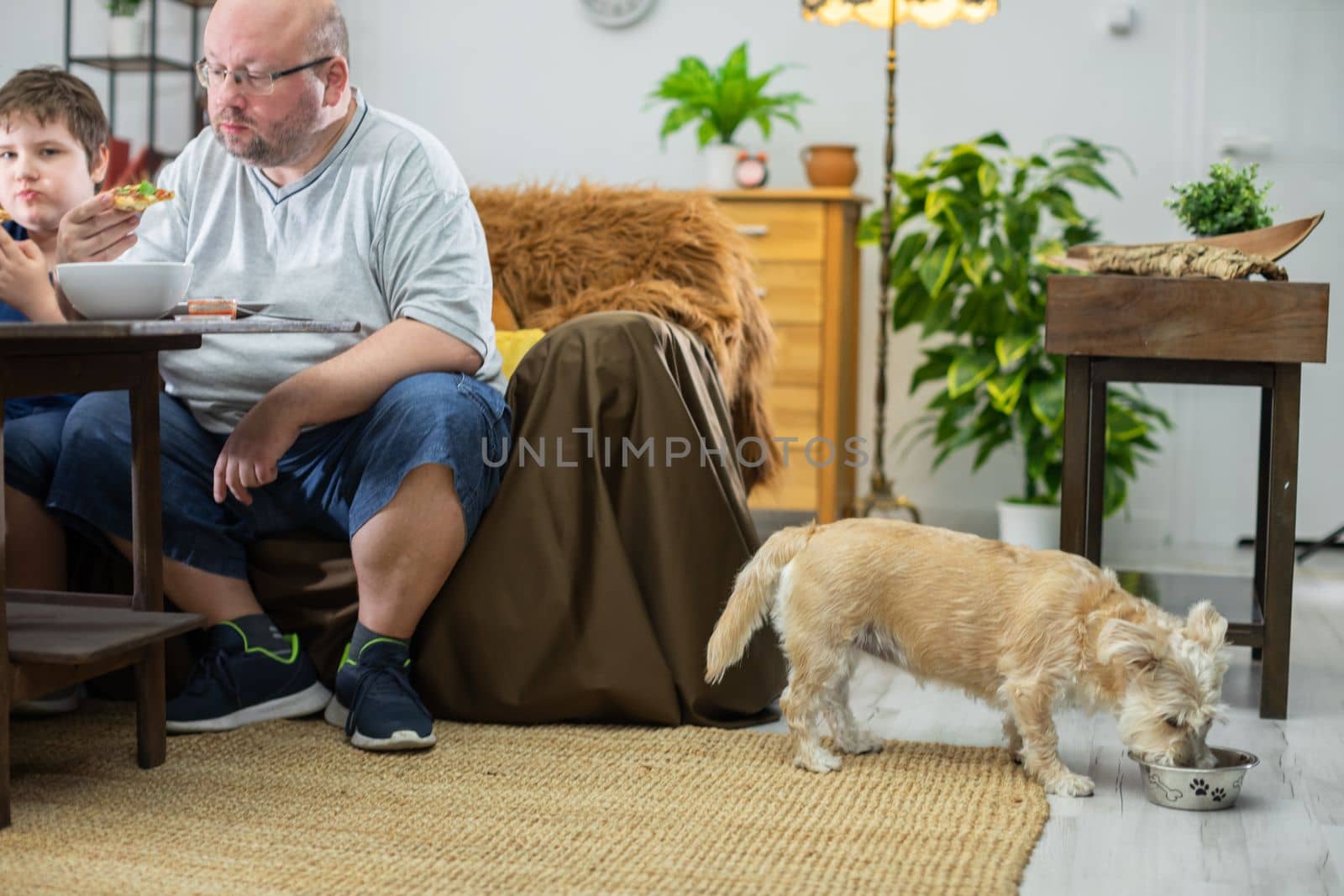 The family eats delicious pizza at the table, while the shaggy pis gets food in his bowl on the floor.