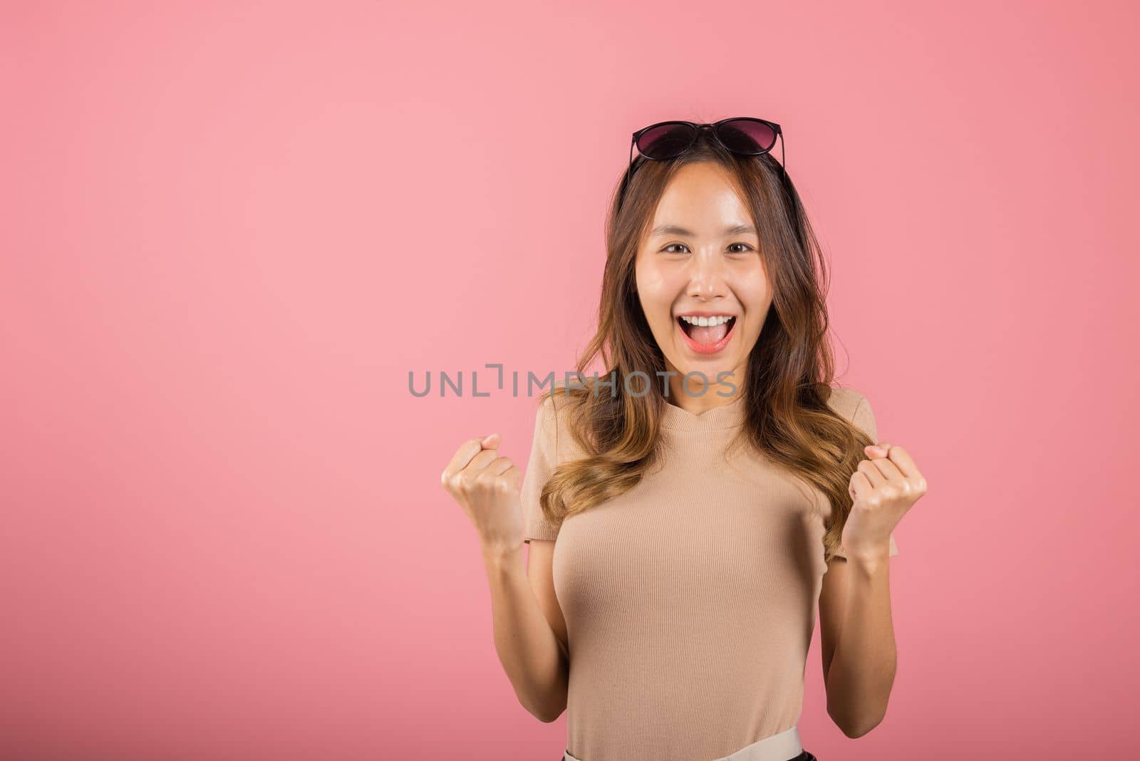 Happy Asian portrait beautiful cute young woman wear glasses makes raised hand up celebrating her winning success gesture, studio shot isolated pink background, Female excited say yes with copy space