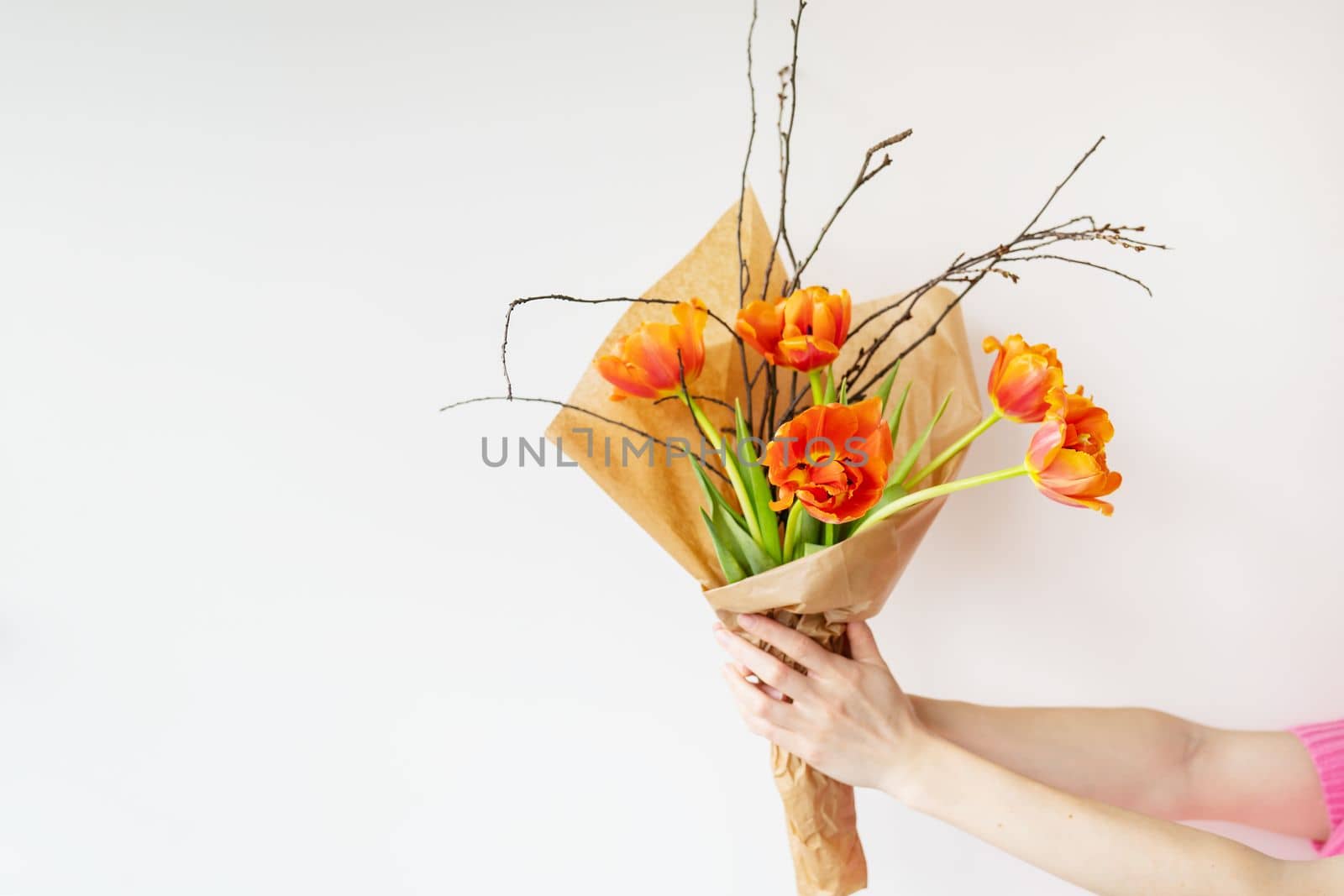 The girl holds in her hands a very beautiful spring bouquet of orange peony tulips along with branches of young cherries